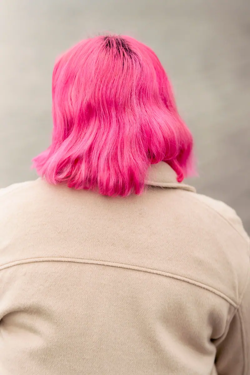 Back view of a woman with bright pink hair sitting peacefully by a lake