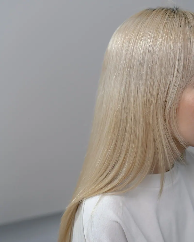Detailed close-up of a woman's blonde hair with a neutral gray background, highlighting texture and color.