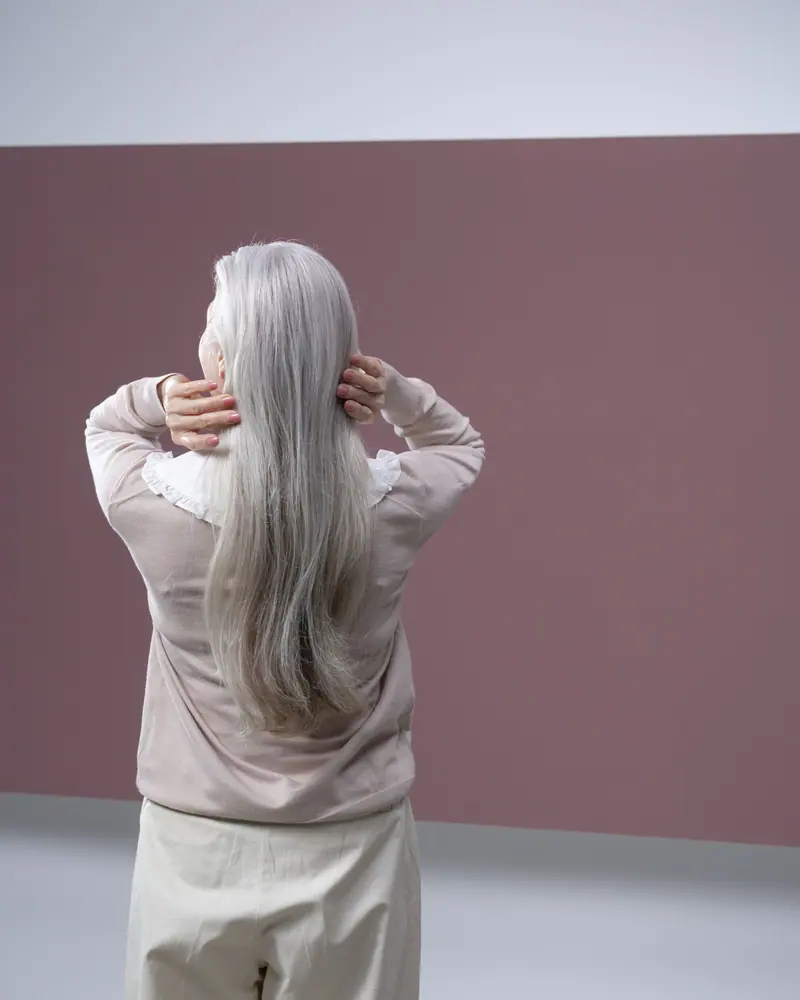 Elegant back view of a senior woman with long silver hair against a neutral background.