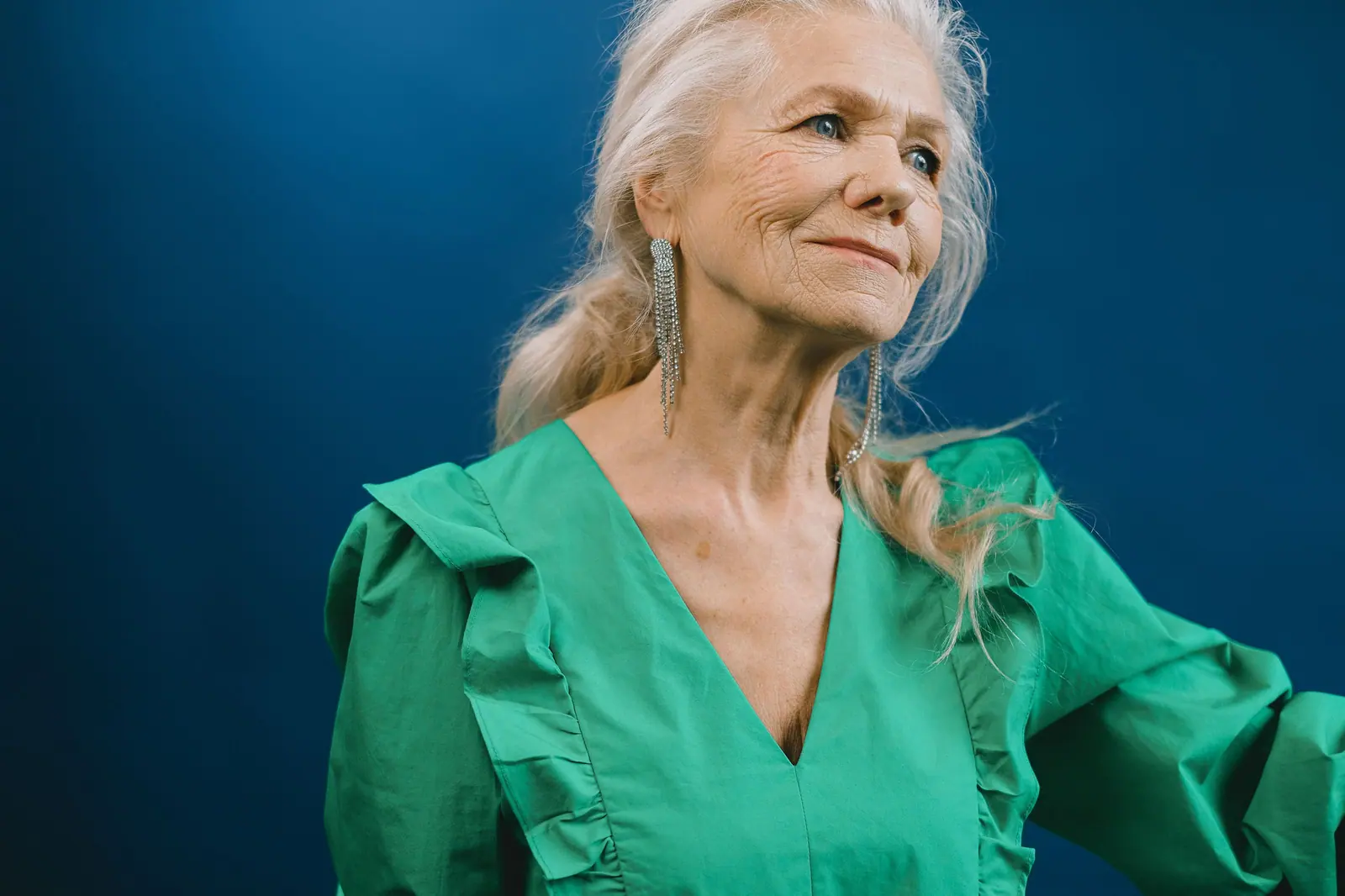 Smiling woman with long silver-blonde hair in a green dress against a deep navy backdrop