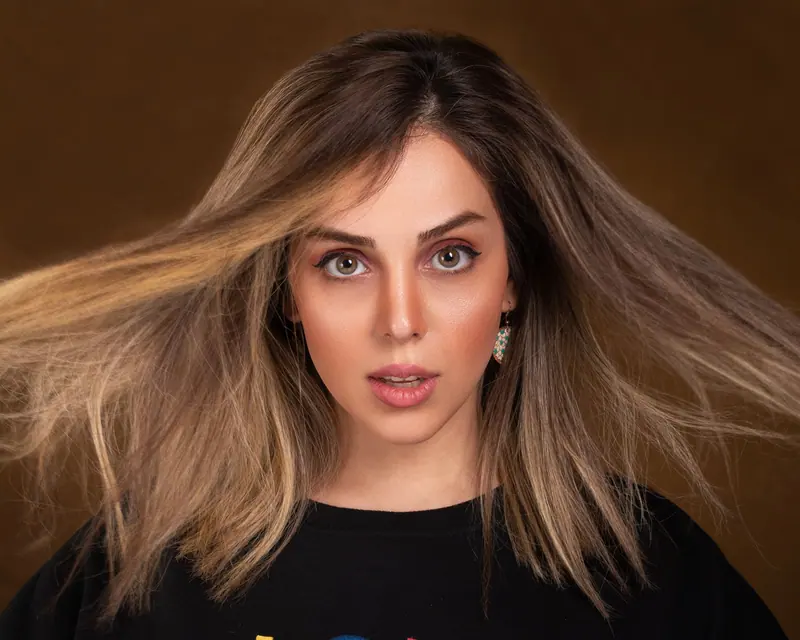 Vibrant studio portrait of a young woman with flying hair and striking green eyes.
