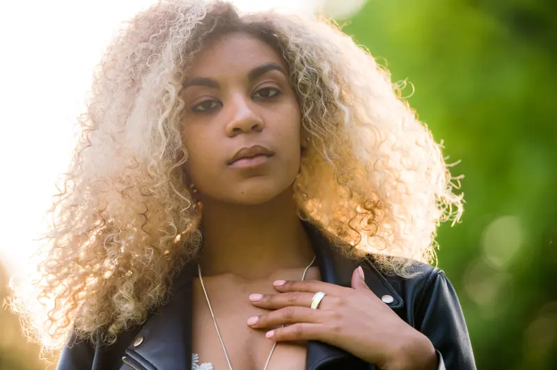 Portrait of a fashionable woman with curly hair and leather jacket enjoying a sunny day outdoors.