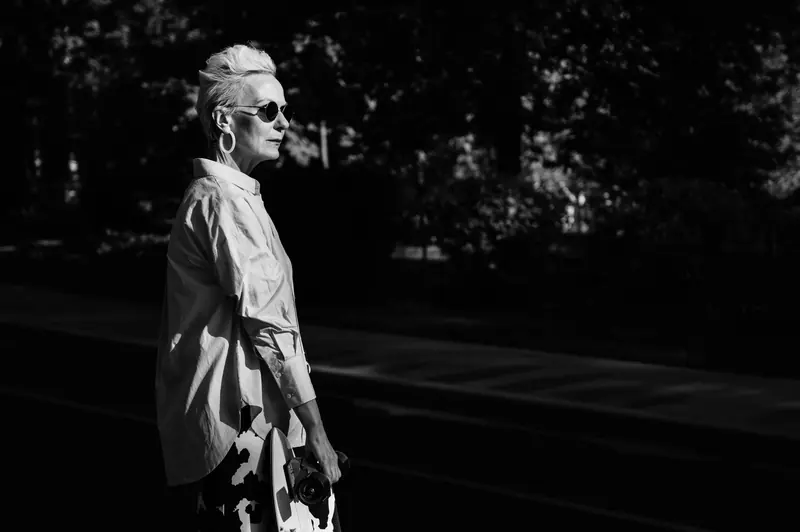 Stylish senior woman wearing sunglasses, captured in a dramatic black and white outdoor setting.