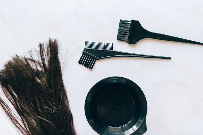 Top view of hair coloring tools and hair strands on a white background.