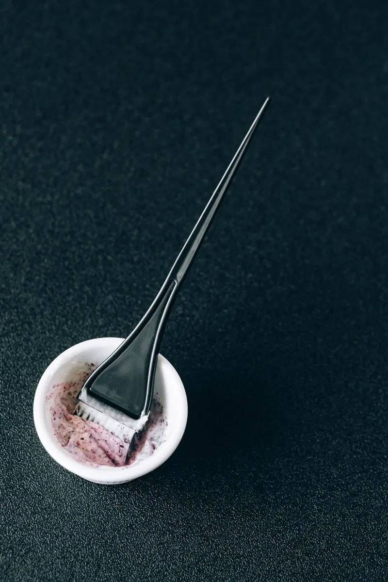 Close-up of a brush and mixing bowl for hair dye on a dark background.