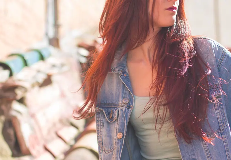 A casual portrait of a young woman with red hair wearing a denim jacket in natural light.