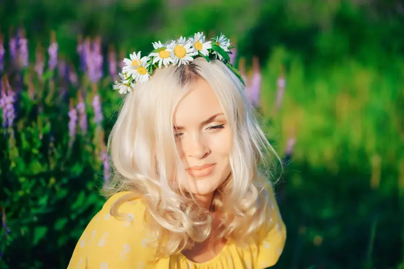 Blonde woman wearing a daisy crown enjoys a sunny day in a vibrant flower garden.