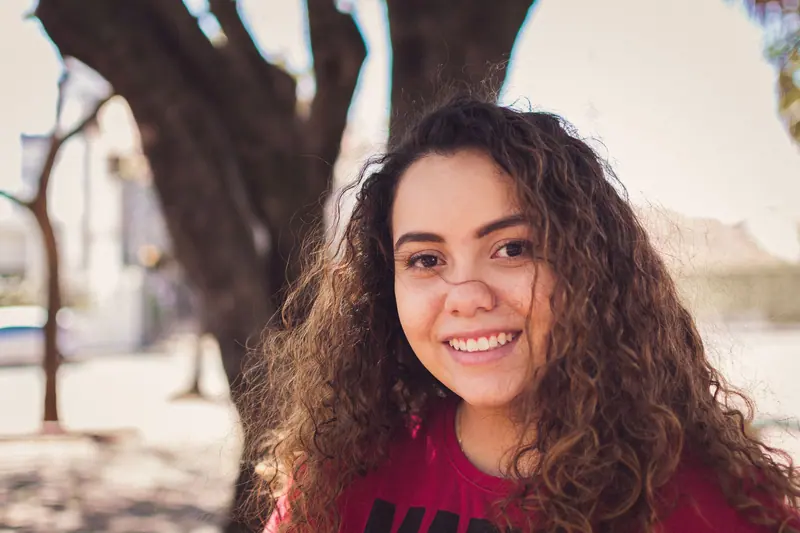 Portrait of a smiling young woman with curly hair in a sunny outdoor setting.