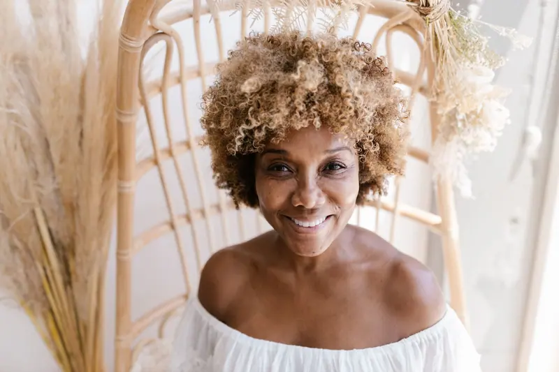 Portrait of a smiling woman with curly hair sitting indoors, exuding warmth and joy.