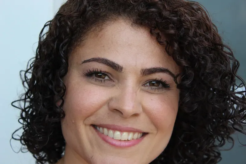 Close-up of a happy woman with curly hair, smiling genuinely outdoors.