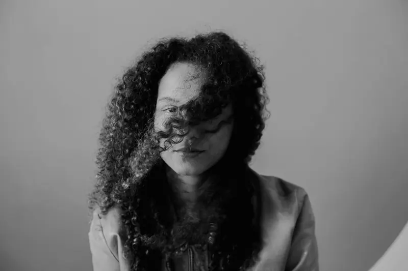 Black and white portrait of a woman with curly hair partially covering her face, creating mystery.