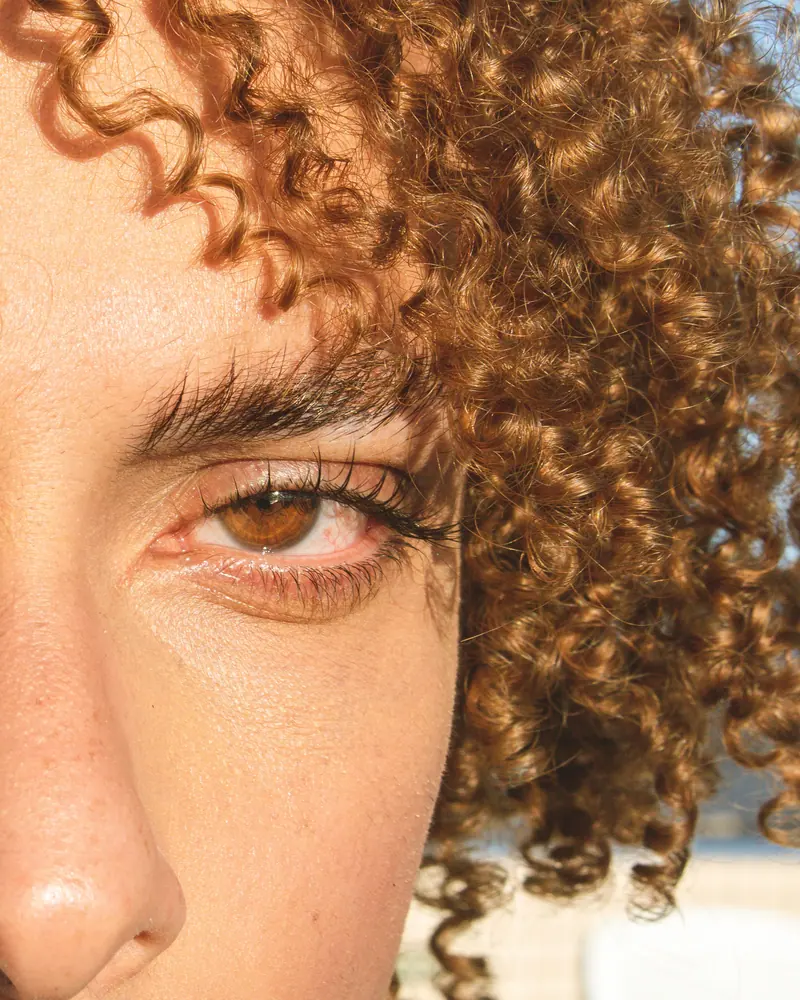 Detailed close-up image of a person's eye with curly blonde hair.
