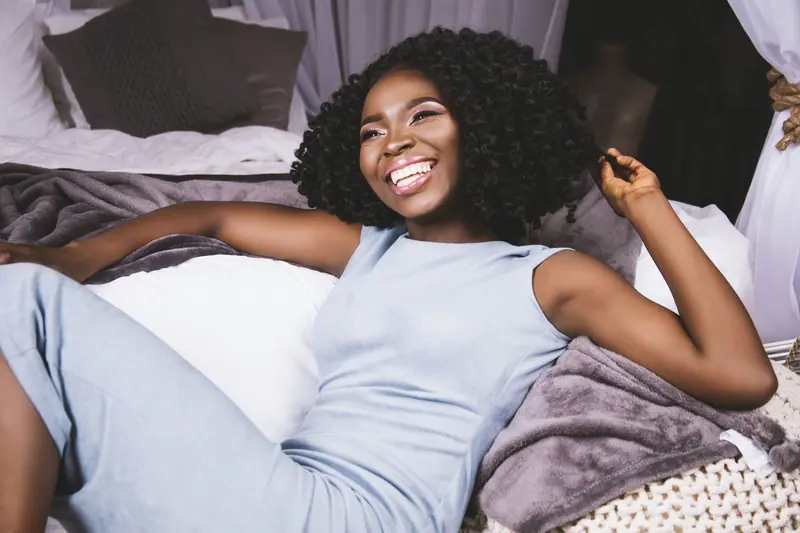 A joyful woman with curly hair relaxing in a comfortable home setting, exuding warmth and contentment.