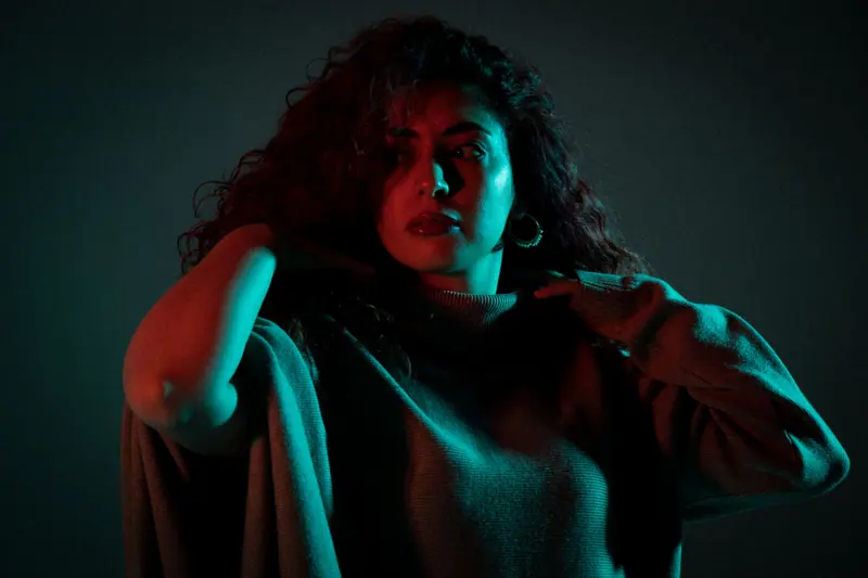 Striking fashion portrait of a woman with curly hair, captured in dramatic lighting and shadows.