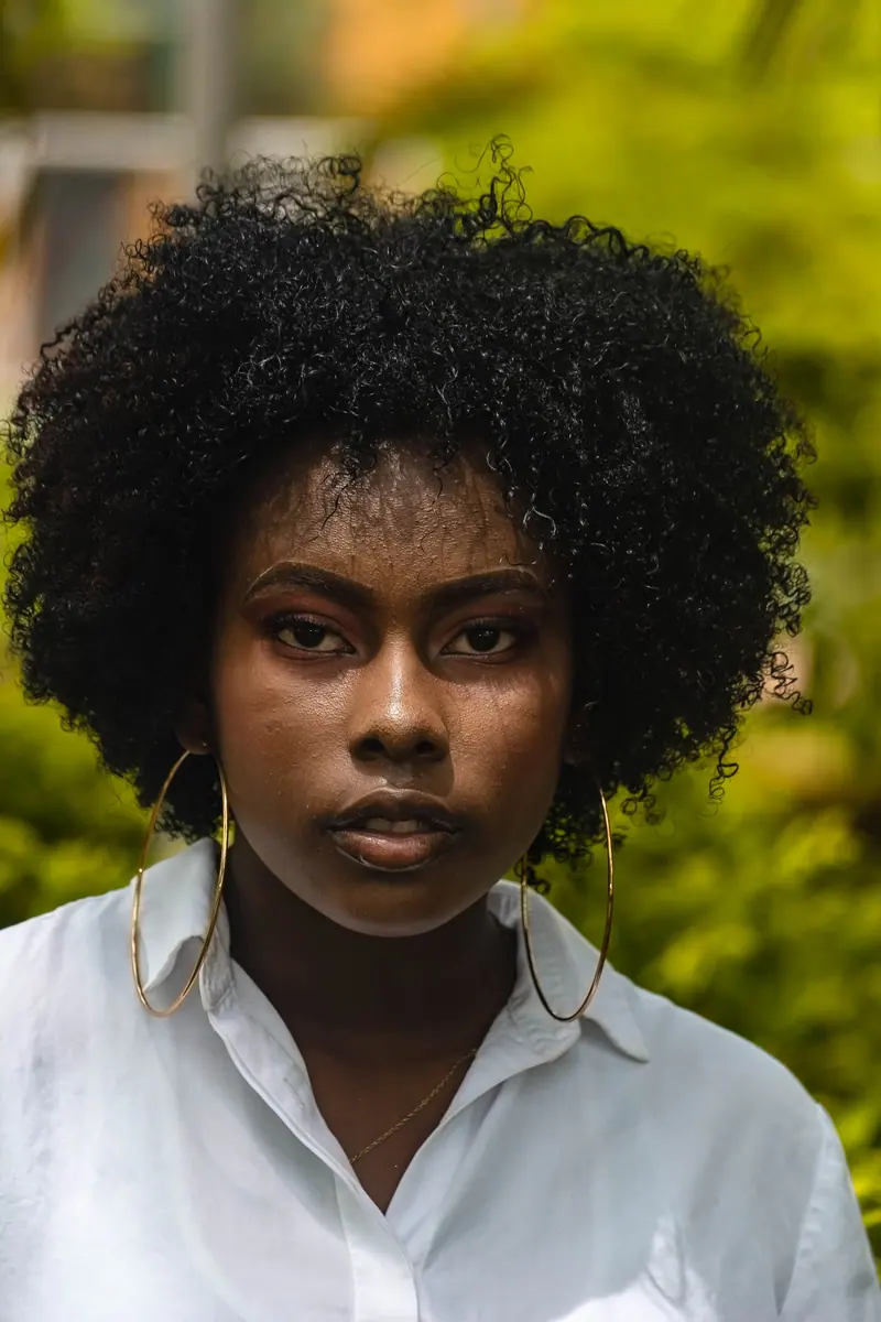Striking portrait of a Black woman with natural curls and hoop earrings against a lush, outdoor backdrop.