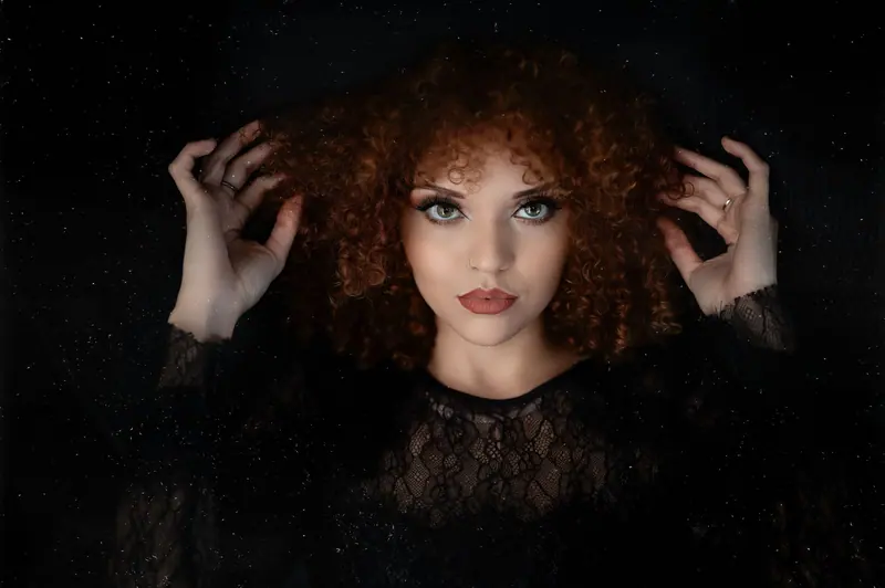 Striking portrait of a woman with curly hair against a black background, exuding elegance and confidence.