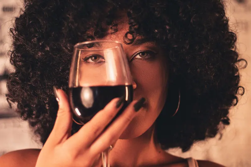 A woman with curly hair enjoys a glass of red wine, exuding elegance and celebration.
