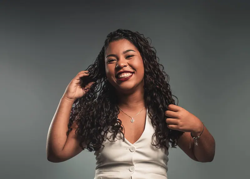 Portrait of a smiling woman with curly hair in a studio setting, exuding confidence and joy.