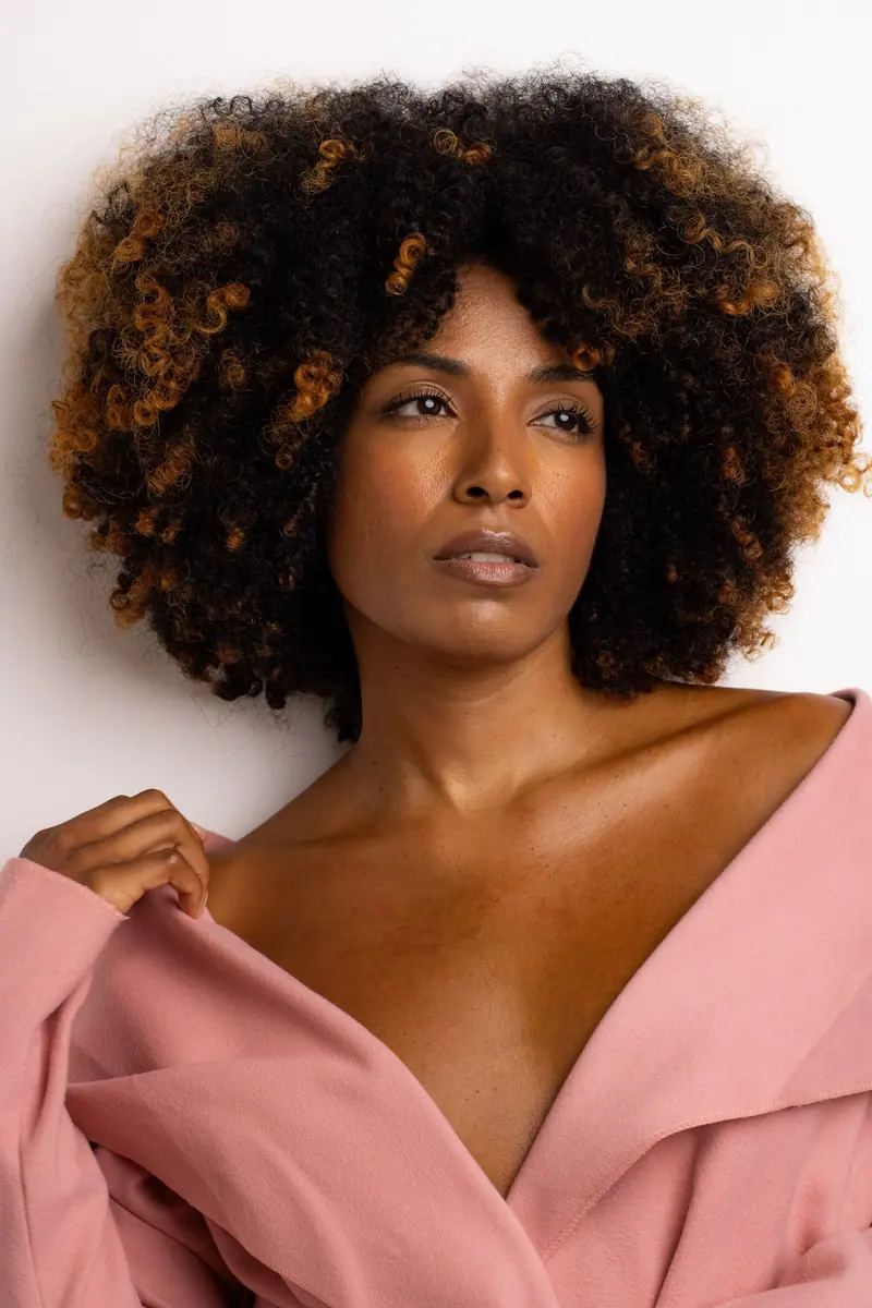 Close-up portrait of a stylish woman with natural curls and a pink outfit, embracing elegance.