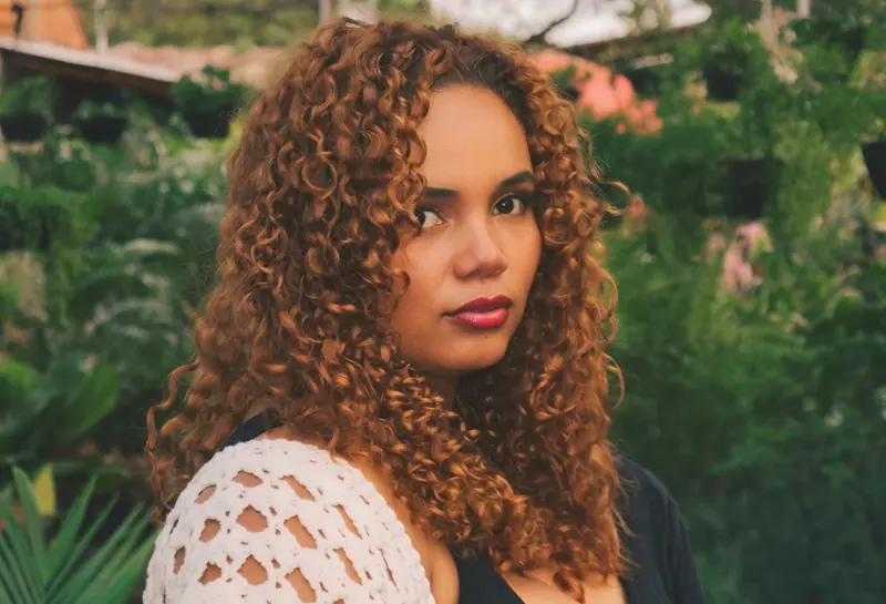 Charming portrait of a woman with curly hair in a vibrant outdoor setting.