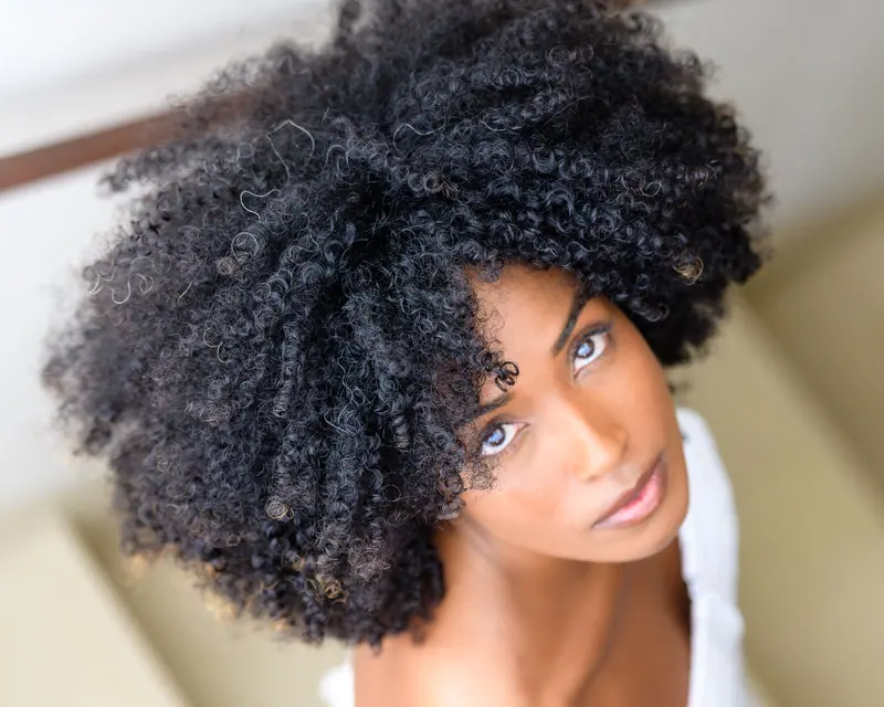 Stunning portrait of a woman showcasing her natural curly afro hairstyle indoors.