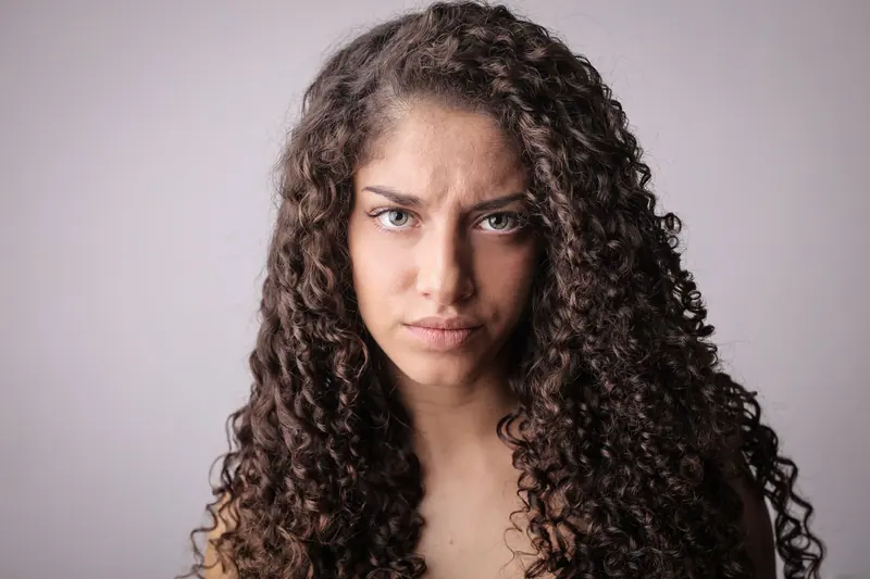 Close-up portrait of a woman with long curly hair and intense expression, isolated on neutral background.