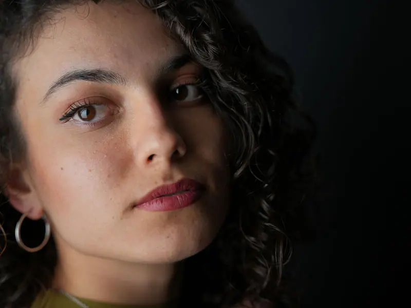A striking close-up portrait of a woman with curly hair, large earrings, and a pensive expression.