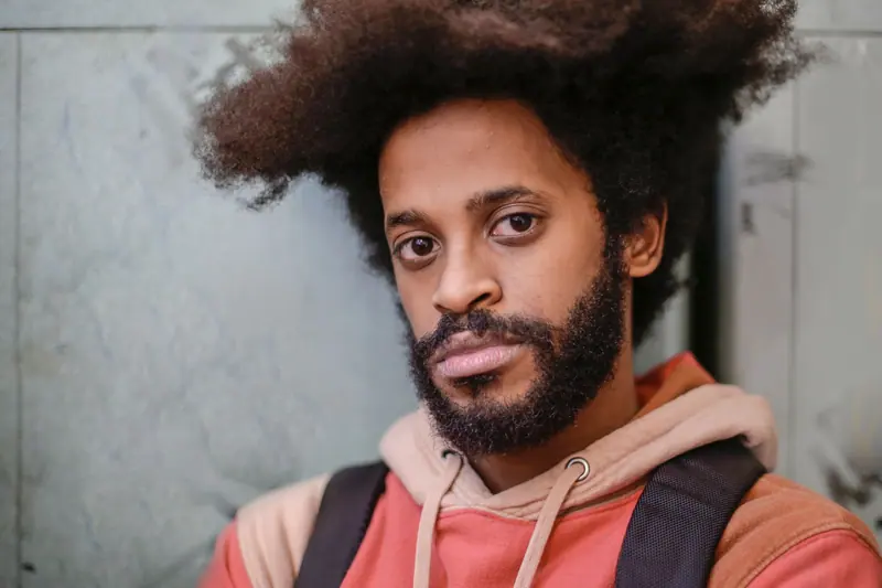 Close-up portrait of a man with an afro hairstyle wearing a hoodie indoors.