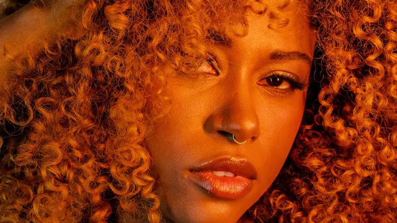 Intimate close-up of a woman with curly hair and jewelry in warm lighting.