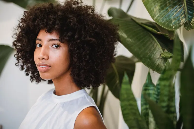 Beautiful portrait of a young woman with natural curly hair in a serene indoor setting with plants.