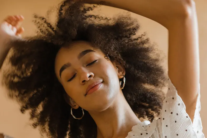 A tranquil studio portrait of a young woman with afro hair and closed eyes, wearing a polka dot dress.
