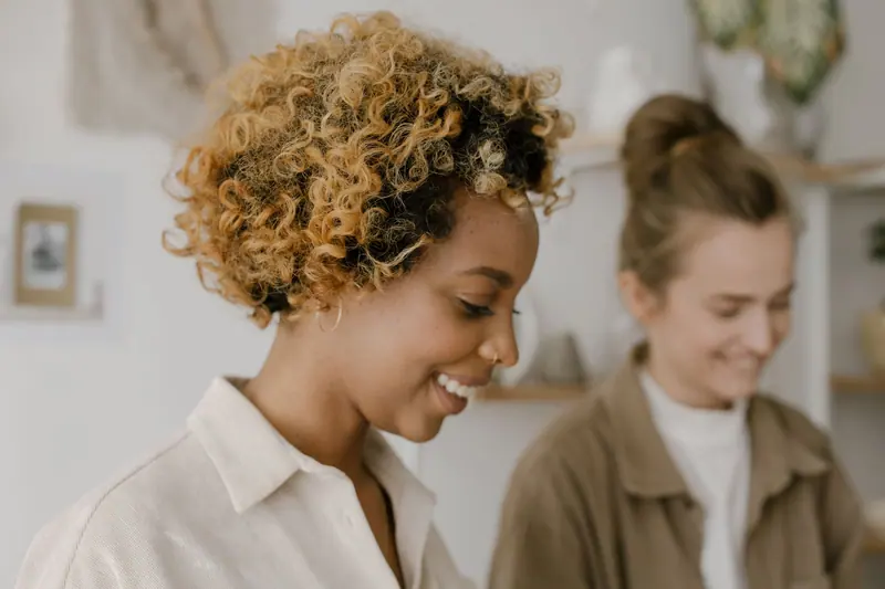 Close-up portrait of two smiling women enjoying a moment indoors with soft lighting.