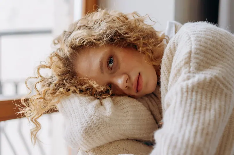 Casual portrait of a relaxed woman with curly hair resting on a pillow wearing a cozy sweater indoors.