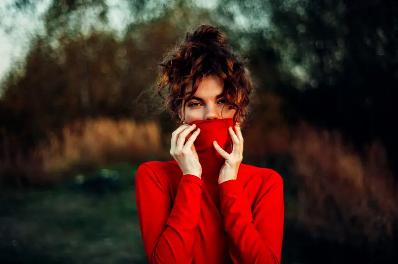 Woman in a red sweater standing outdoors with mystery and allure.