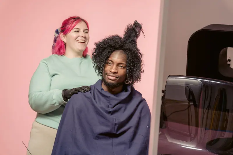 Hairdresser joyfully styles client's hair in a modern studio, showcasing diversity and professionalism.