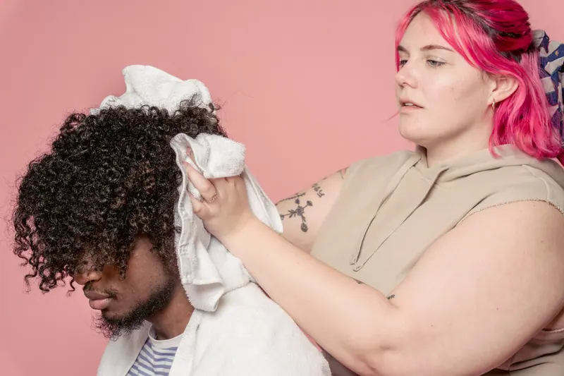 Hairdresser drying male client's curly hair with a towel in studio.