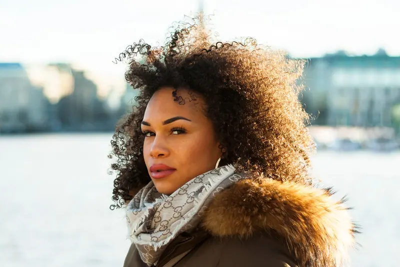 Portrait of a fashionable woman with curly hair and scarf by Hamburg's waterfront.
