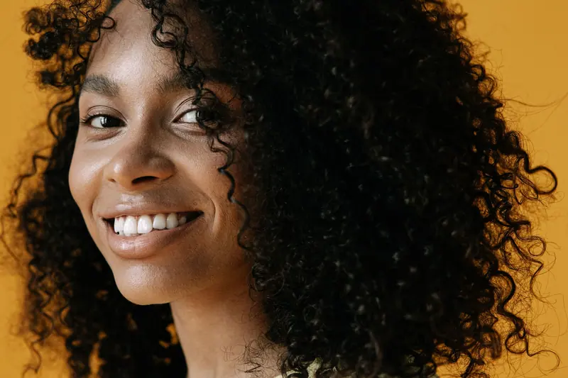 Close-up portrait of a smiling woman with curly hair against a yellow background.