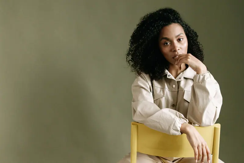 Thoughtful woman with curly hair sitting on a chair in a studio.