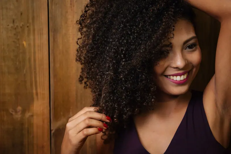 Close-up portrait of a smiling woman with curly hair touching her locks indoors.