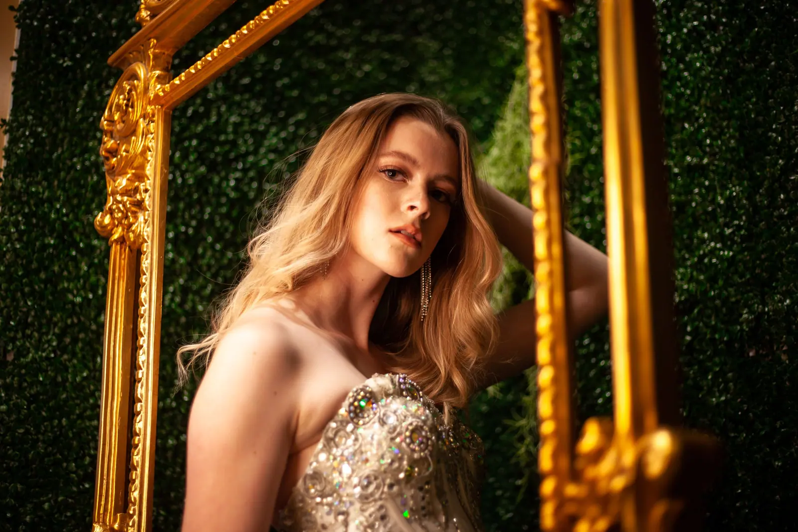 Woman with long golden waves posed beside an ornate gilded mirror