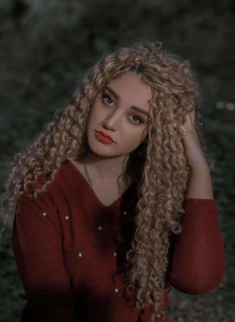 A beautiful portrait of a woman with long curly hair and red attire in an outdoor setting.