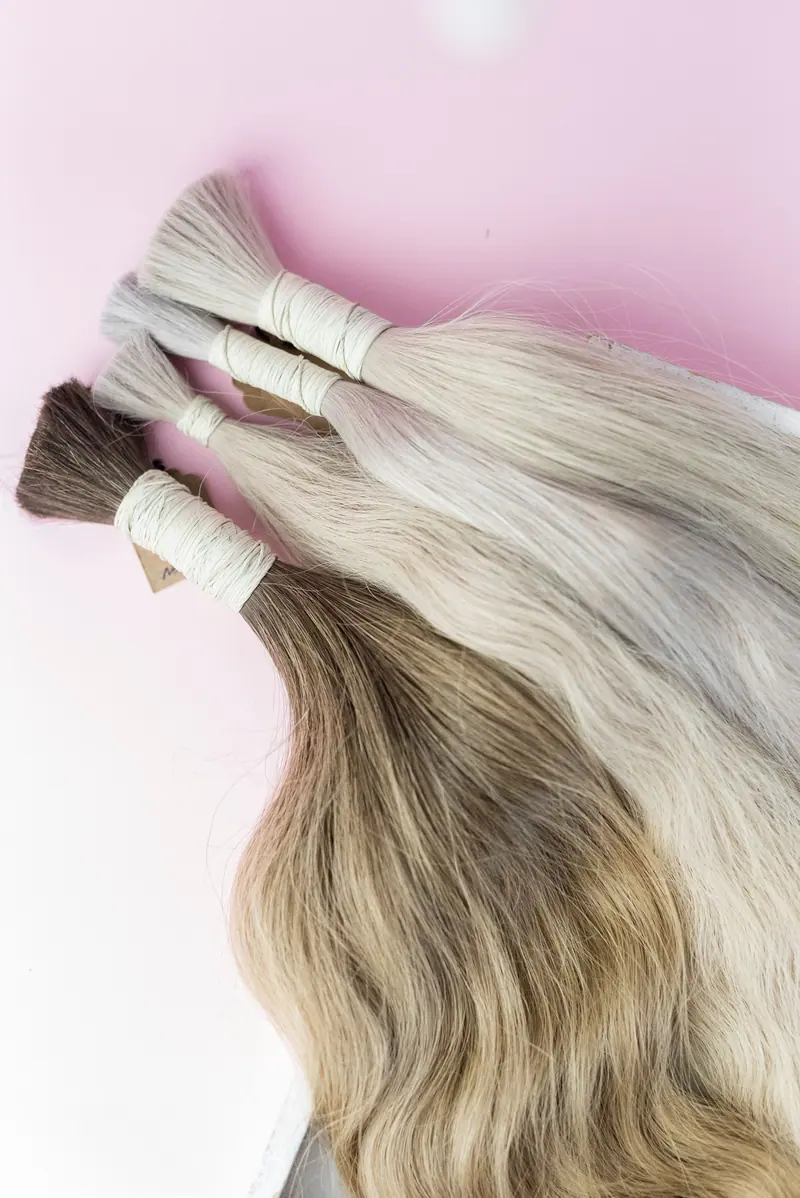 Bundles of blonde extension hair on a pink backdrop
