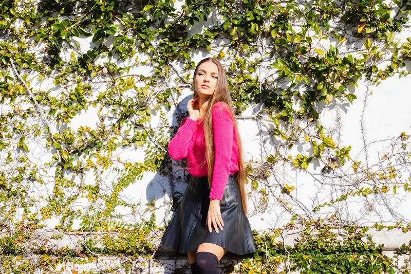 Long hair and a pink jacket against an ivy wall