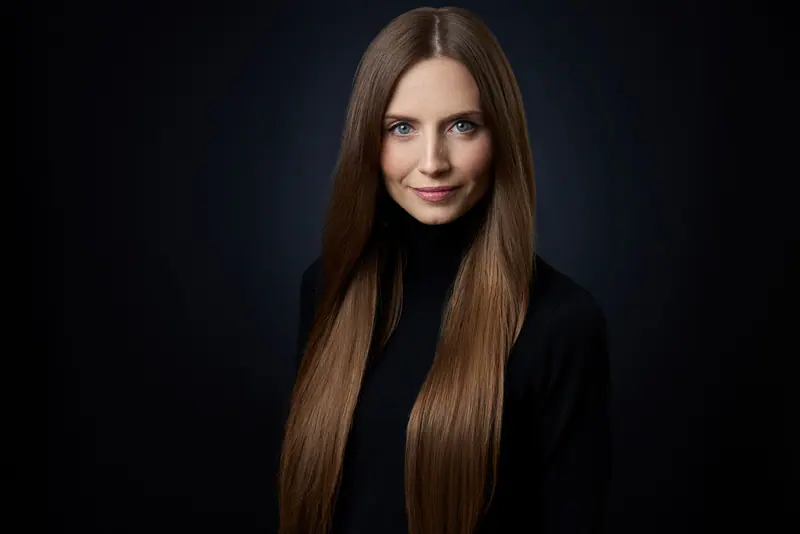 Studio portrait of a brunette woman with long hair in black outfit.