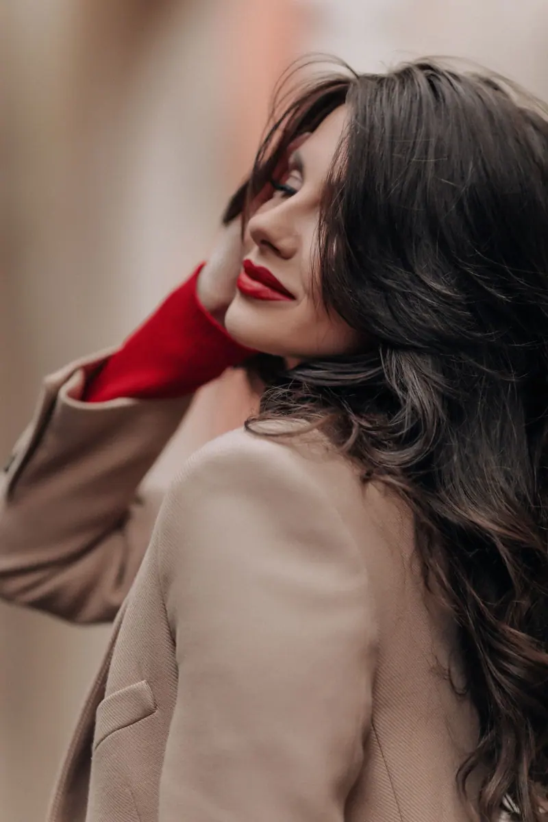 Stylish brunette woman posing elegantly in a beige coat, showcasing long hair and a modern fashion style.