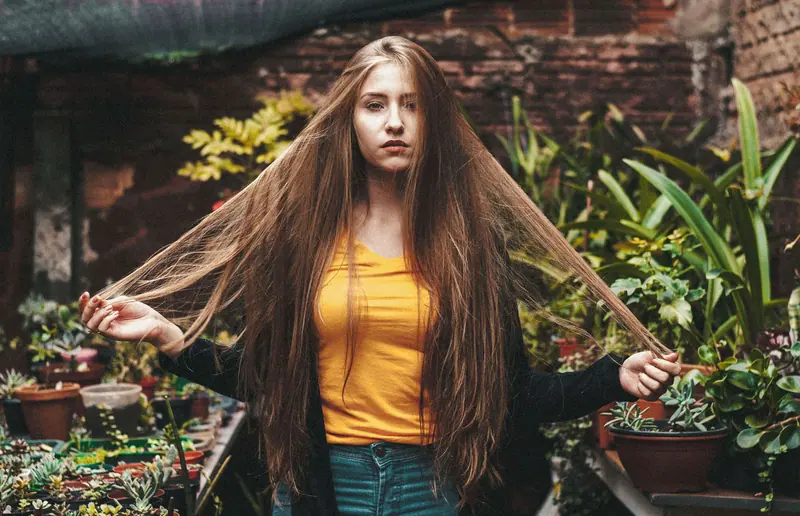 Portrait of a young woman with long brown hair posing in a lush garden setting.