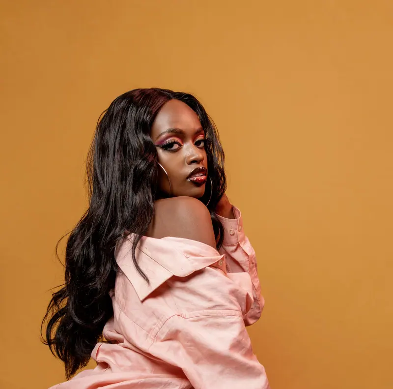 Woman with long glossy waves in a pink shirt against a saffron backdrop
