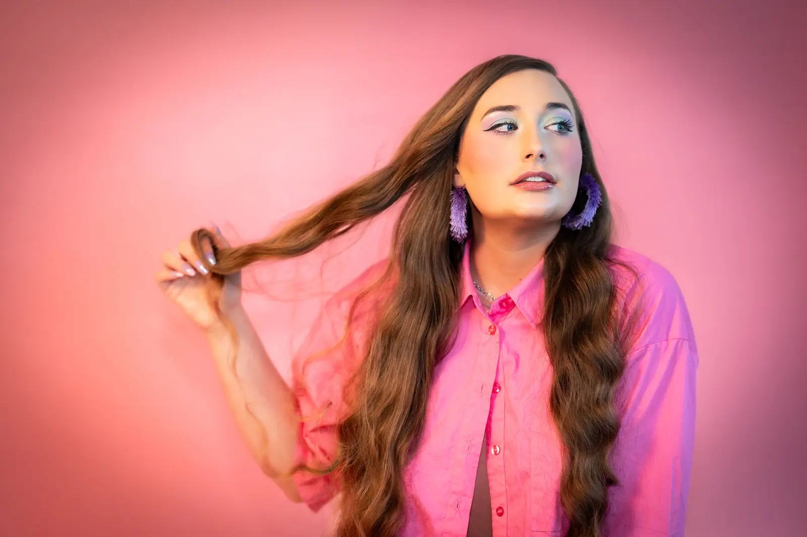 Woman twirling long, wavy brunette hair against a rosy pink backdrop