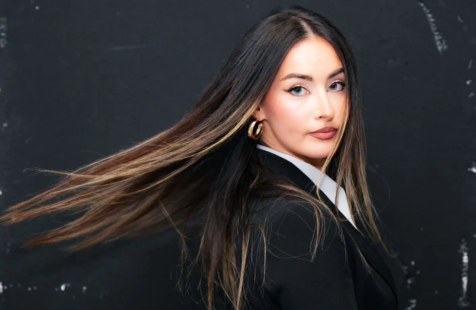 Long dark hair whipping sideways against a near-black background